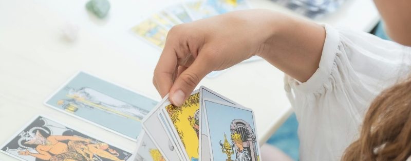 Ilustracja do sesji Rozmowy z kartami. Na zdjęciu profil kobiety rozkładającej karty tarota na białym stole